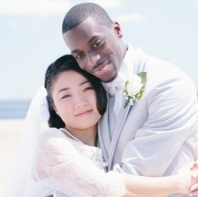 Portrait of bride and bridegroom on beach looking at camera hugging, smiling